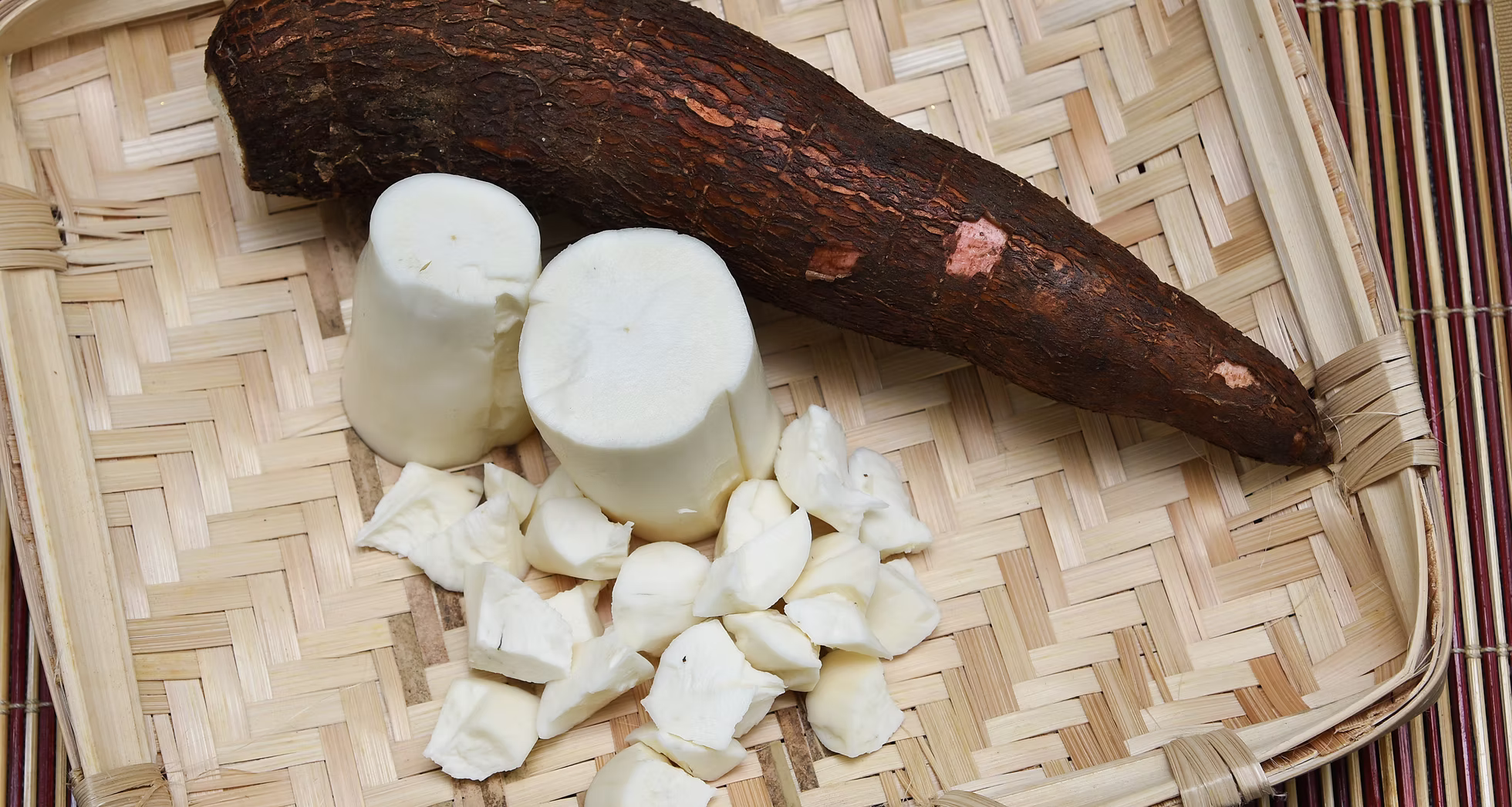 Cassava root with peeled white pieces arranged on a woven bamboo tray